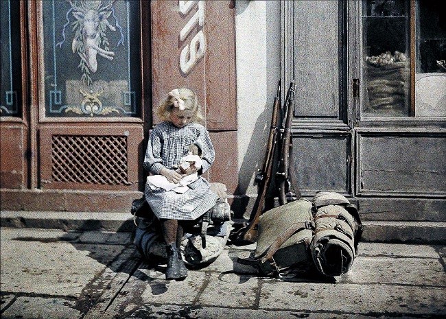 Girl Holds a Doll Next To Soldiers Equipment